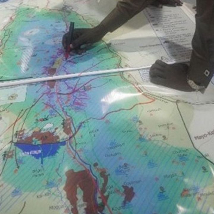 A big map on a table and hands tracing the map with pen and ruler.