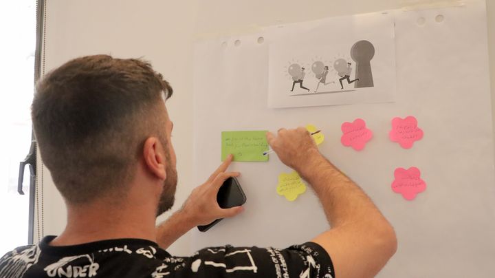 A person from the back writing on a small paper sticking on a white board.