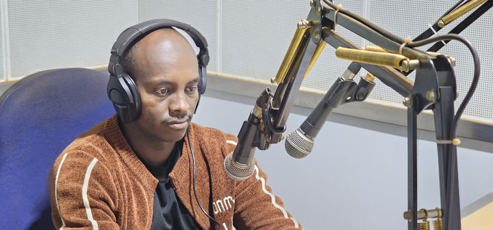 A man with headphones sitting in front of a microphone in a radio studio.